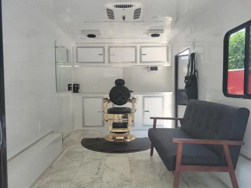 Barbershop trailer interior with a gold and black barber chair, a gray waiting sofa, white cabinets and a marble-look floor