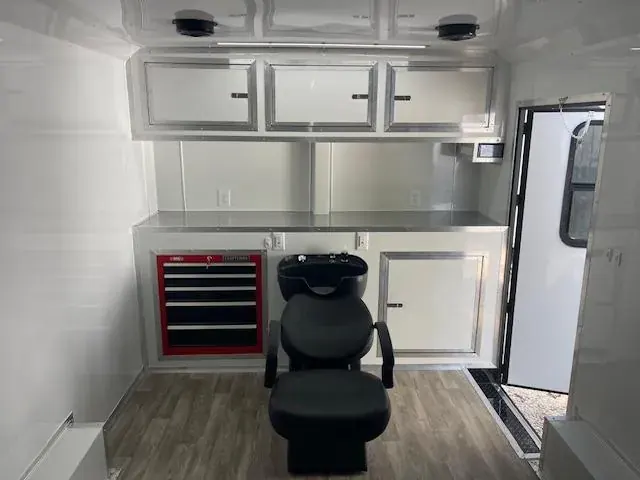 Barbershop trailer interior with a black shampoo chair, red Craftsman tool drawers, white cabinets and a counter