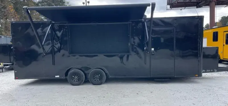 Black tandem-axle concession trailer with a large awning service window propped open, on a gravel lot