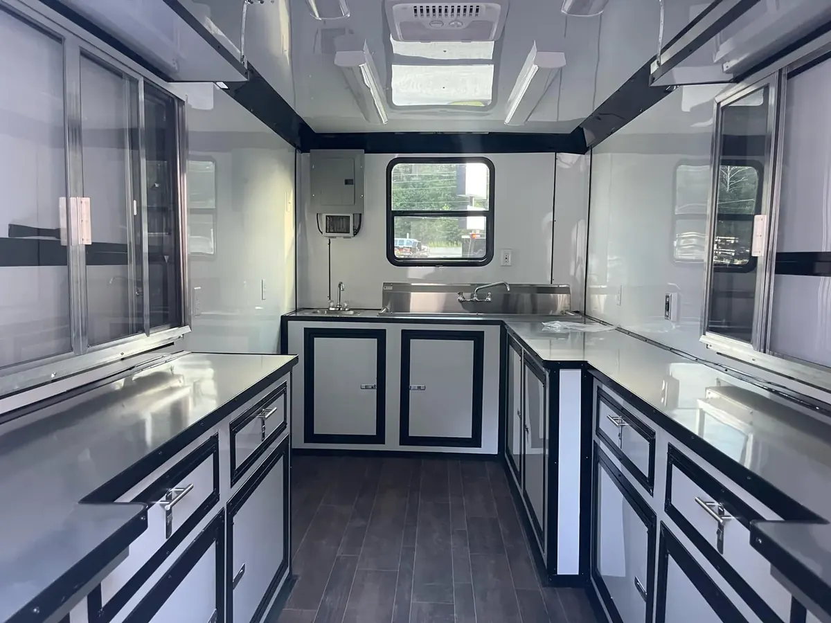 Concession trailer interior with white and black cabinets, stainless steel counters, sinks, serving windows and an air conditioner