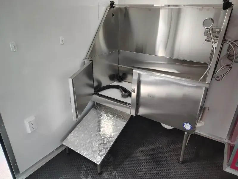 Close-up of a stainless steel dog grooming tub with a diamond-plate step and white walls