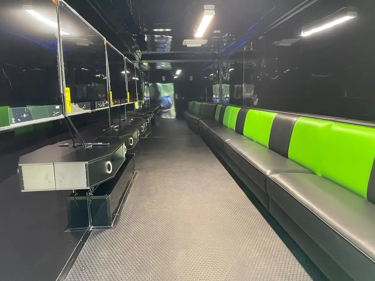 Video game trailer interior with a row of wall-mounted TVs over console stations on the left and green and black bench seating on the right