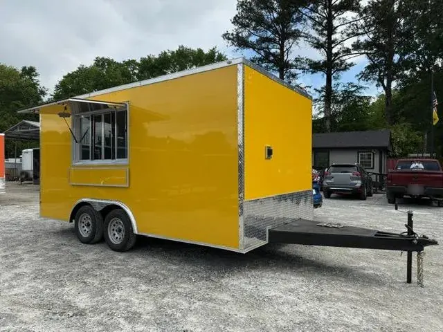 Yellow tandem-axle concession trailer with a serving window and awning, parked on a gravel lot